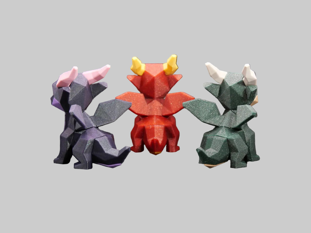 Three low-poly dragon figurines in purple, red, and green, displayed on a dark surface with a black background.
