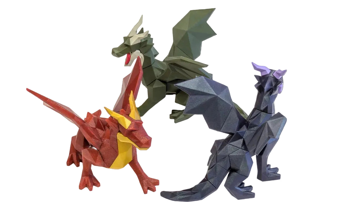 Three low-poly dragon paper model toys in red, green, and dark blue-gray are displayed on a clean white background.