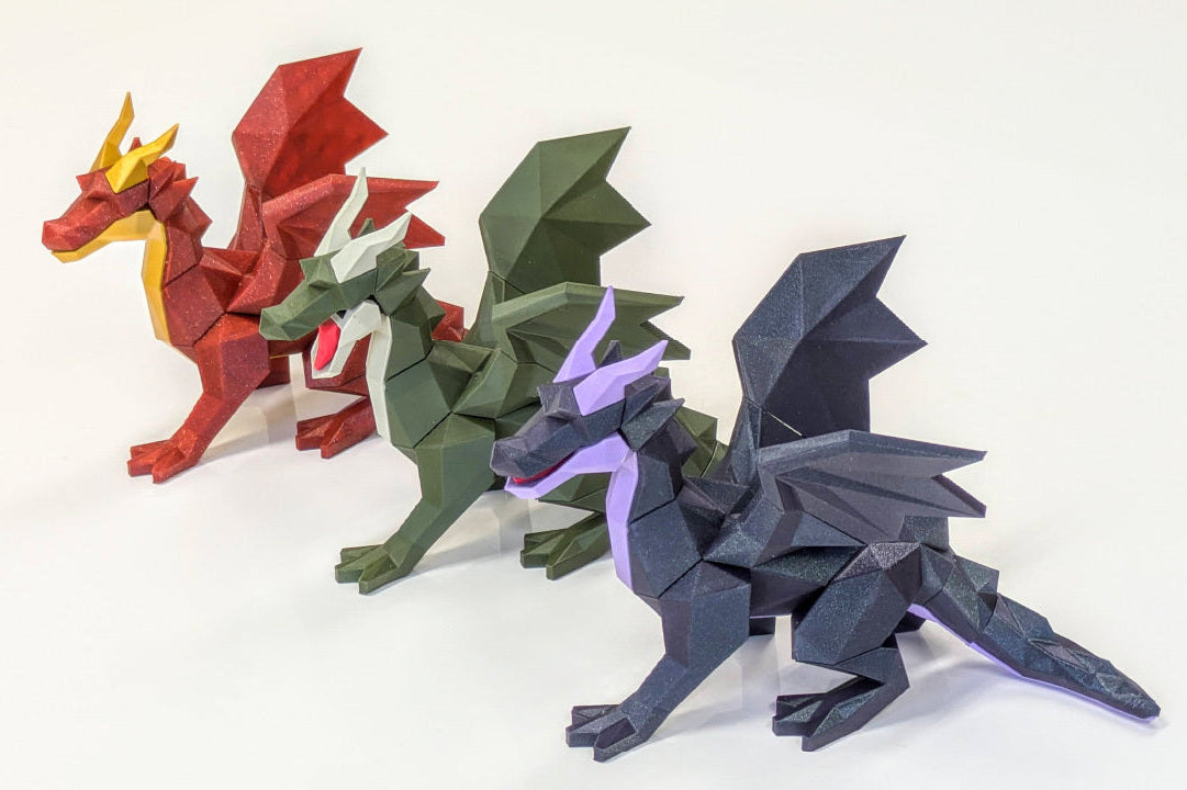 Three low-poly paper dragon models in red, green, and dark gray are arranged diagonally on a white background.